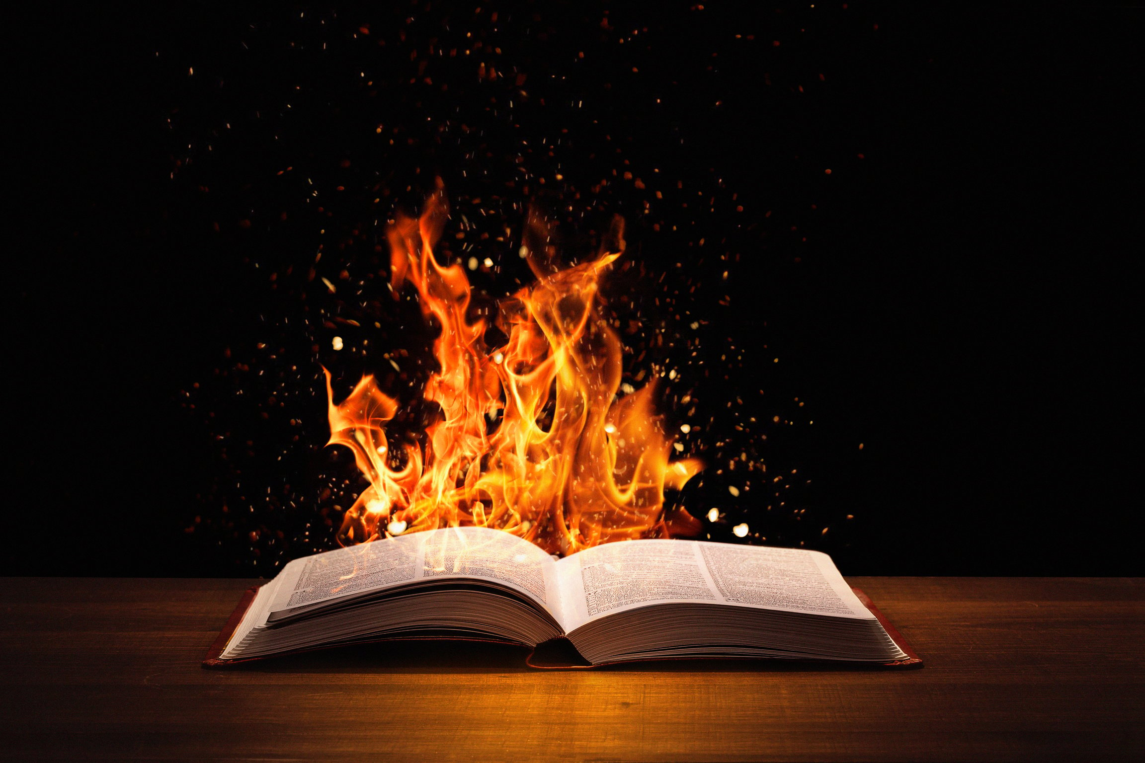 Holy Bible on fire on a wooded desk